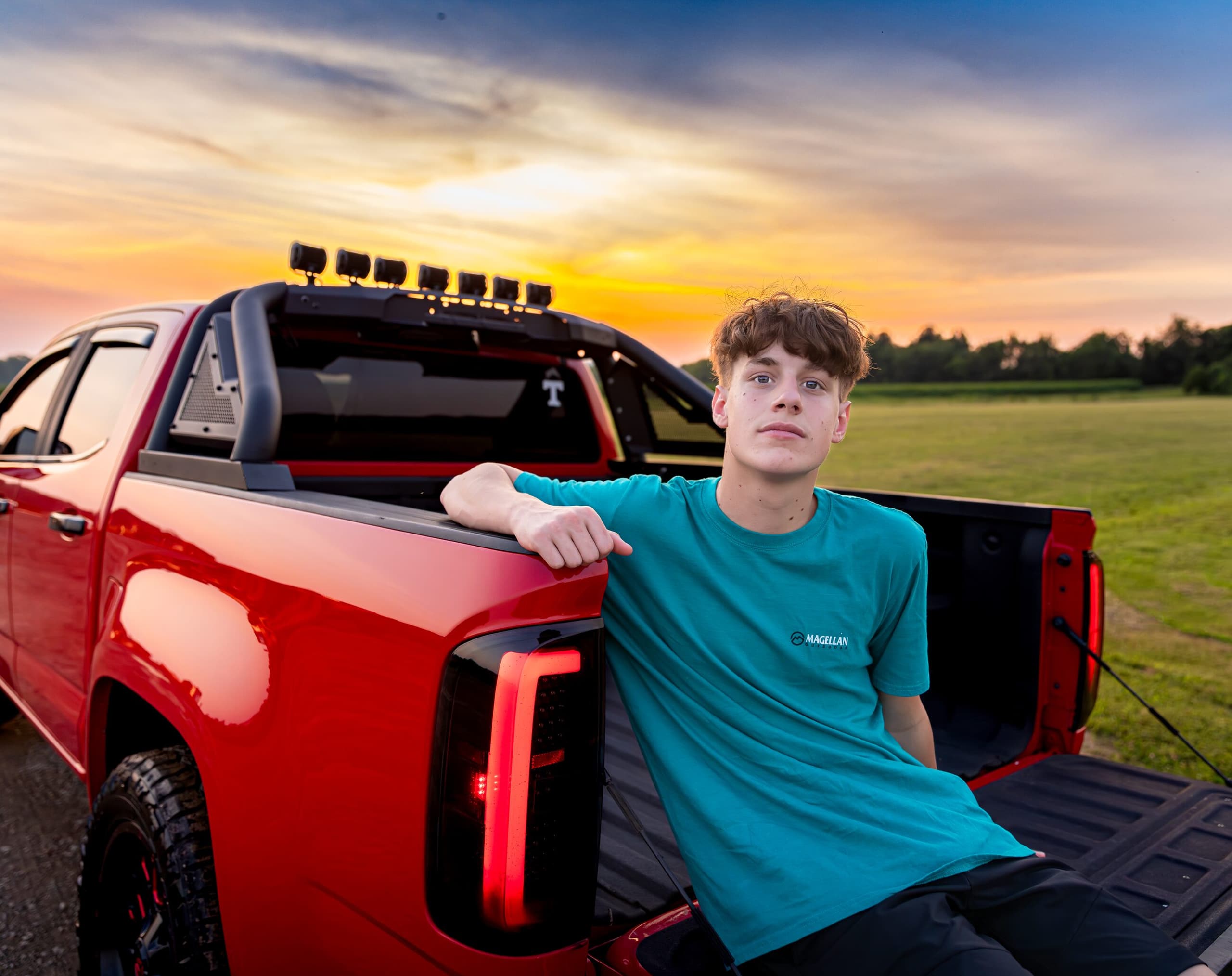 Senior portrait on a red pickup tailgate at sunset